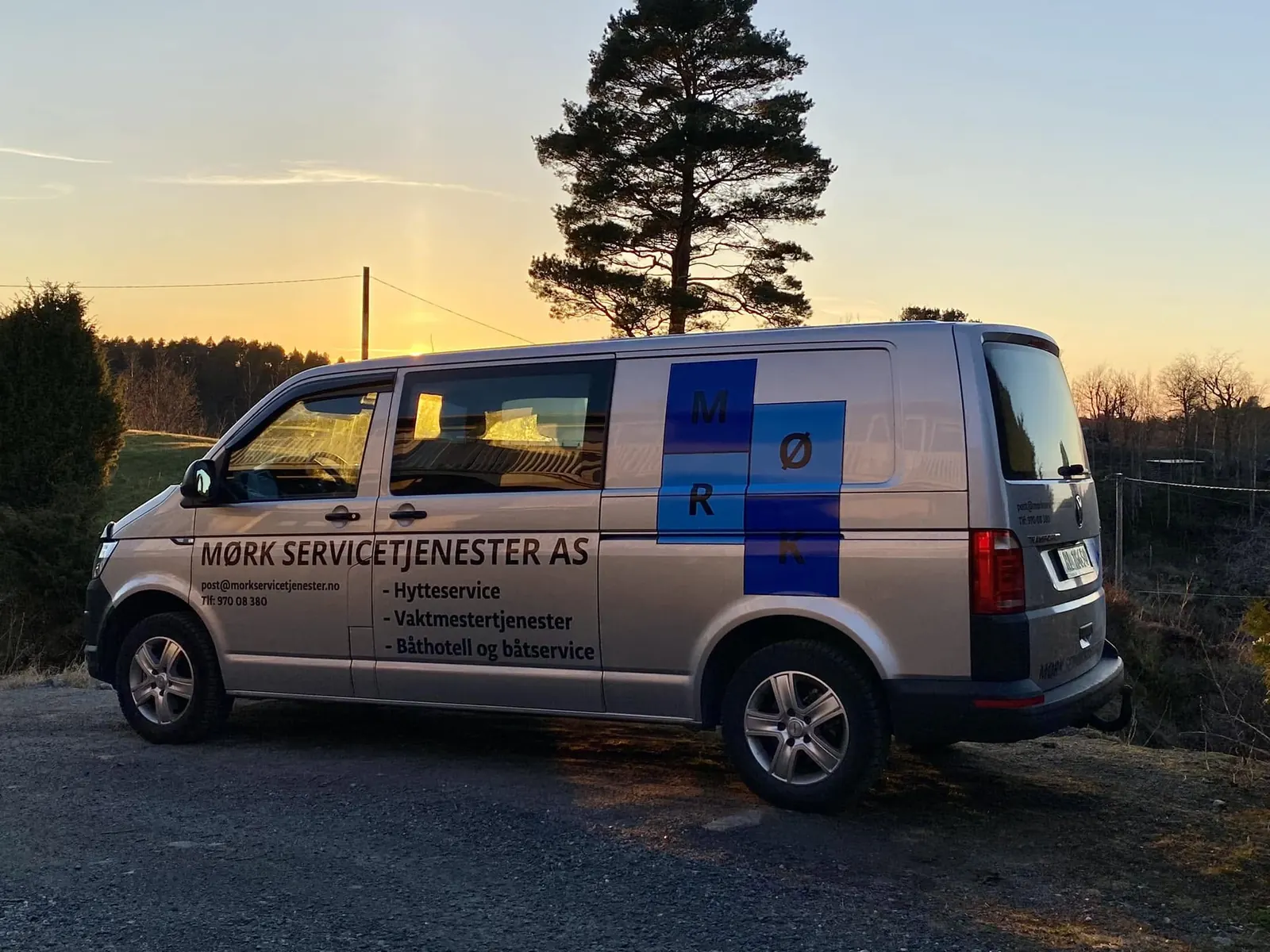 Firmabilen til Mørk Servicetjenester AS parkert i solnedgang, merket med hytteservice og vaktmestertjenester