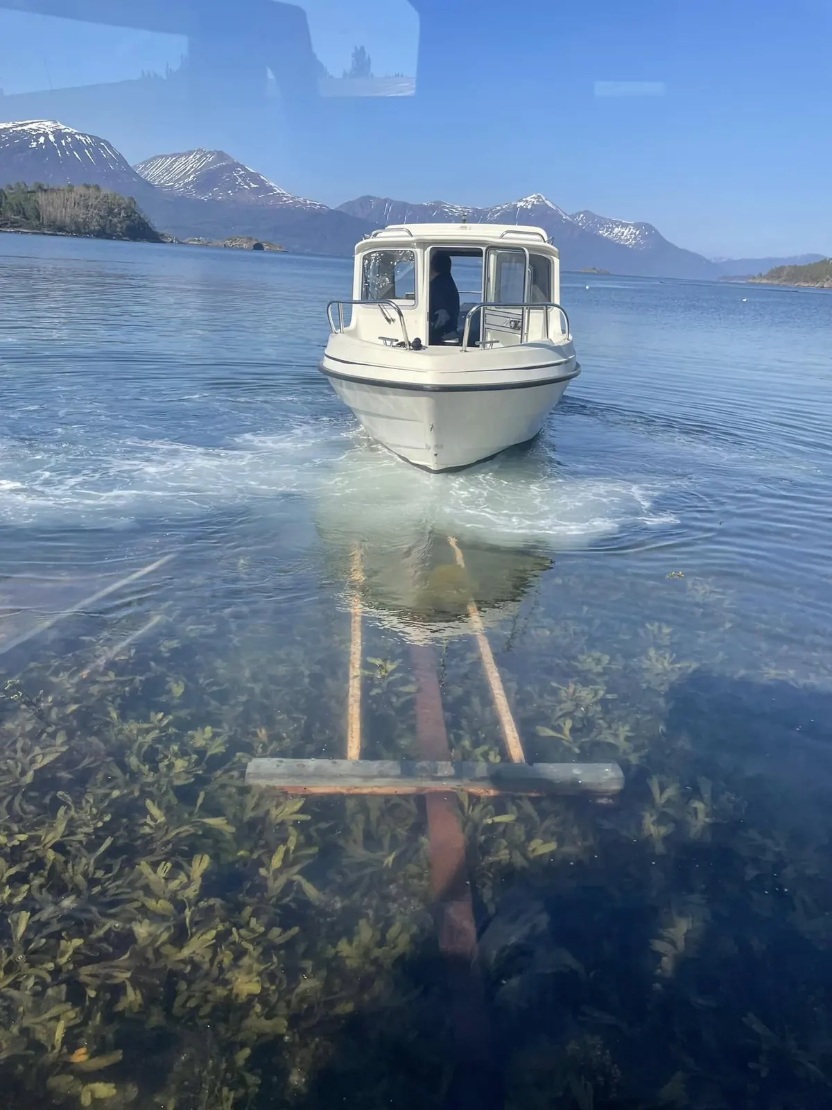 Hvit kabinbåt på slippskinnene i klart vann med snødekte fjell bak