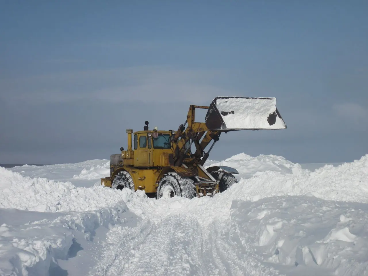 Gul hjullaster med hevet skuffe som brøyter dyp snø
